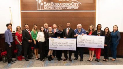 Representatives from San Bernardino City School District hold large checks