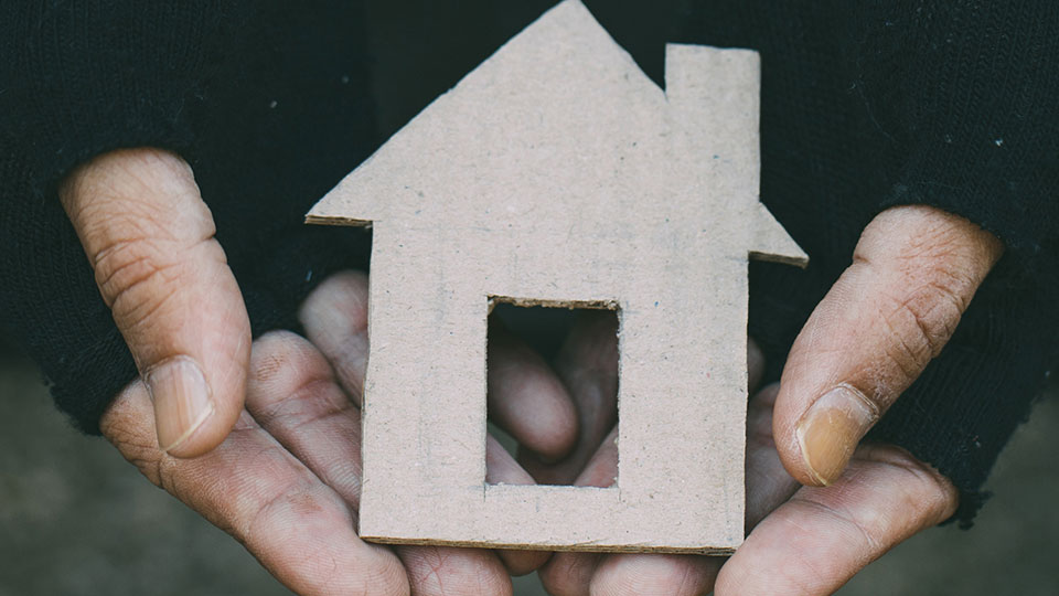 Homeless man's hands holding a paper cutout of a house