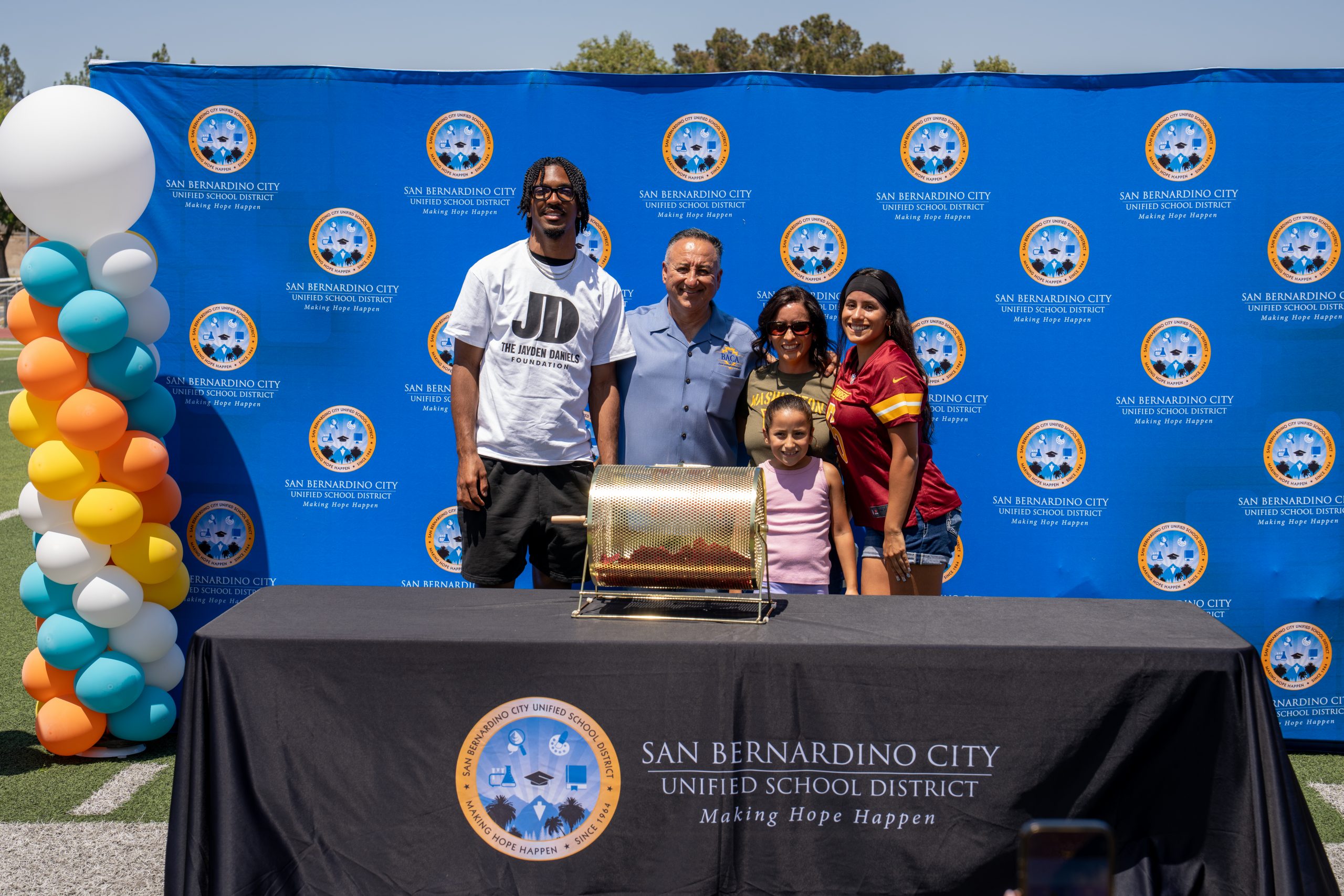 Supervisor Joe Bac, Jr. posing for a photo with his wife, two daughters, and Washington Commanders Quarterback Jayden Daniels at his first Community Day at Cajon High.