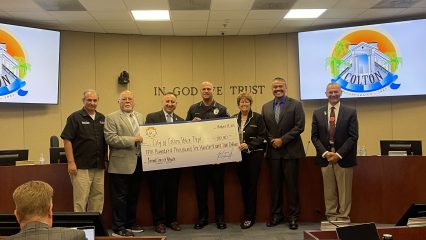 Supervisor Joe Baca, Jr. stands with Colton city leaders and the Colton Police Department inside the City Council Chambers, presenting a large ceremonial check for $100,000 to support the purchase of a new animal care services vehicle.