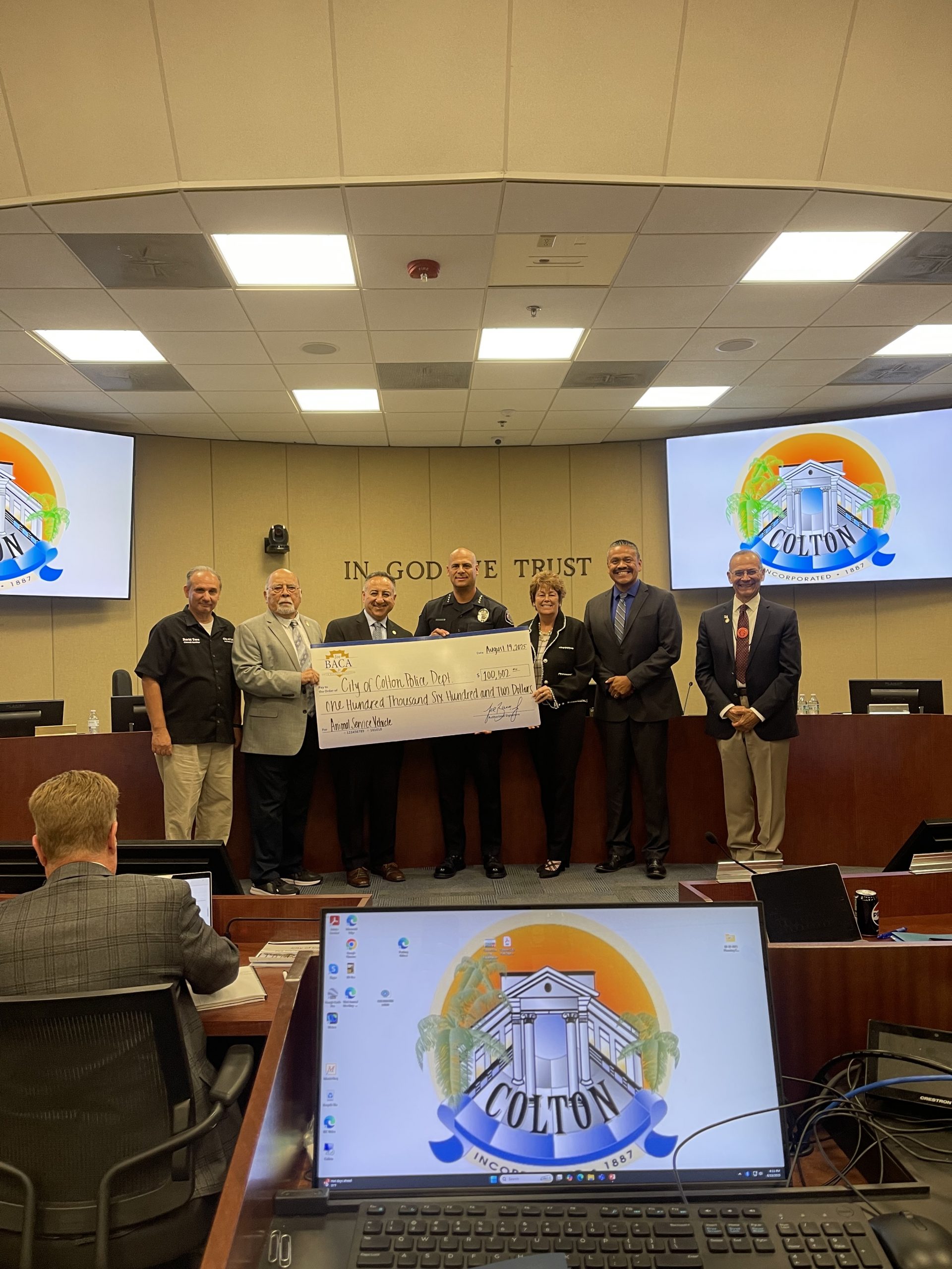 Supervisor Joe Baca, Jr. stands with Colton city leaders and the Colton Police Department inside the City Council Chambers, presenting a large ceremonial check for $100,000 to support the purchase of a new animal care services vehicle.
