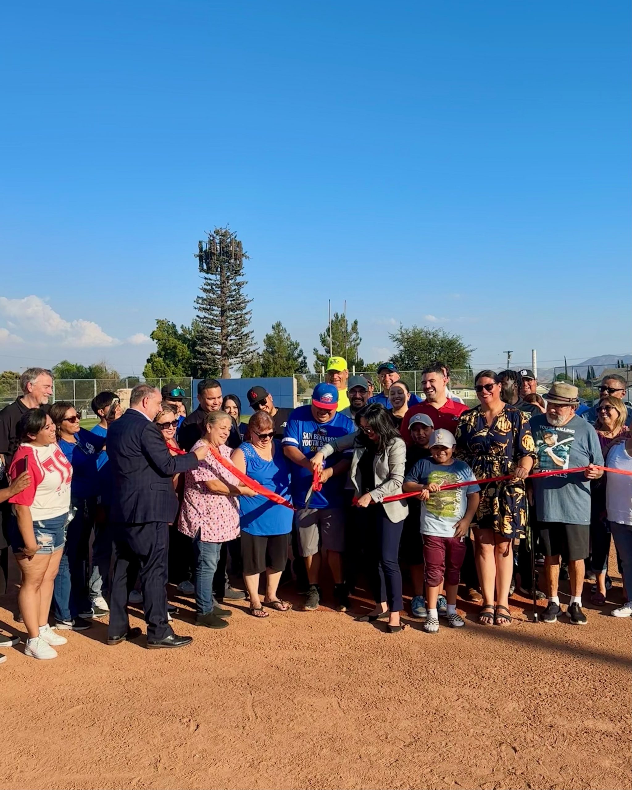Supervisor Joe Baca, Jr., San Bernardino Mayor Helen Tran, representatives from Senator Reyes’ office, and members of the San Bernardino Pony League join community residents for a ribbon cutting ceremony celebrating the reopening of Guadalupe Field. The group gathers on the baseball diamond, smiling as they cut the red ribbon together.